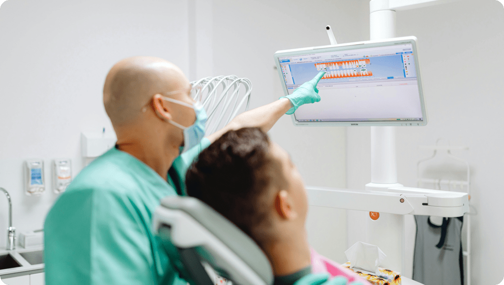 Dentist discussing a patient's dental treatment plan using a digital 3D teeth model displayed on a computer monitor in the dental clinic.